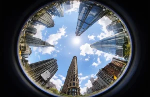 Fisheye lens view of city skyscrapers curving inward around the sky, demonstrating extreme wide-angle distortion and circular 360 degree perspective from ground level