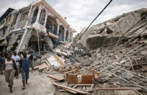 Hyper-realistic scene of the 2010 Haiti earthquake aftermath in Port-au-Prince, showing collapsed buildings, massive piles of rubble, damaged streets, and people walking through the destruction following the disaster